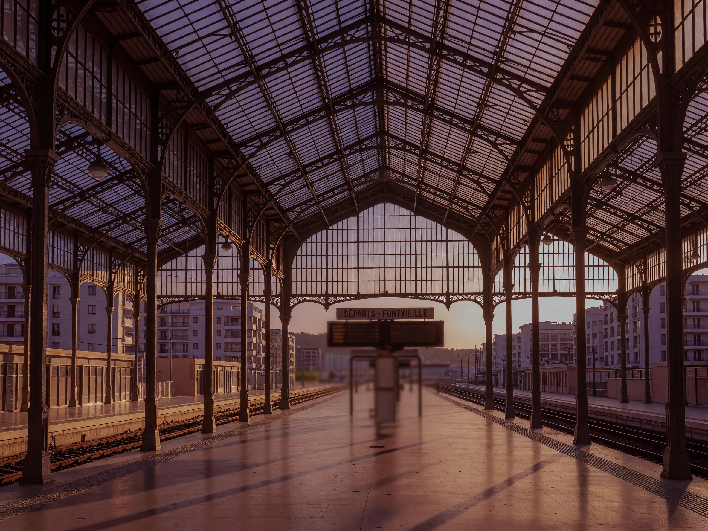 Empty Monte Carlo train station platform with Victorian glass architecture and golden hour light.